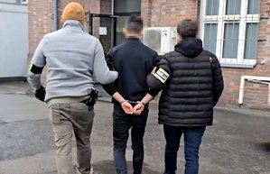 na zdjęciu dwóch nieumundurowanych policjantów prowadzi zatrzymanego mężczyznę