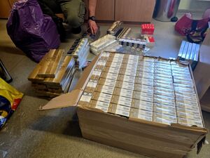 leżący na podłodze karton z paczkami papierosów obok policjant wykładający z torby wagony papierosów