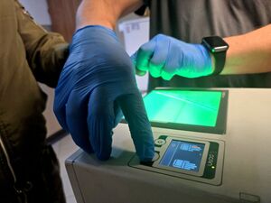 dłonie w niebieskich rękawiczkach przy urządzeniu do daktyloskopii