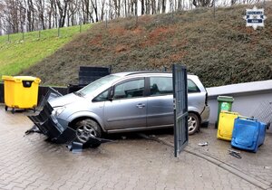 samochód osobowy srebrnego koloru, przy skarpie, przed nim uszkodzone przęsło ogrodzenia i przewrócone kontenery na odpady