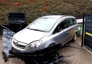 samochód osobowy srebrnego koloru, przy skarpie, przed nim uszkodzone przęsło ogrodzenia