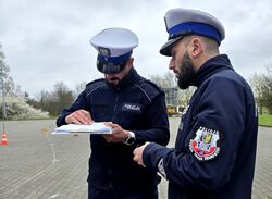 widzimy dwóch policjantów drogówki, jeden z nich trzyma arkusz i długopis w dłoniach