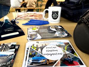 ulotki, długopisy, kubek, kaski policjantów leżące na stoliku
