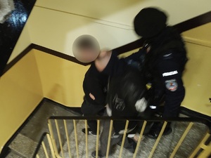Zdjęcie przedstawia zatrzymanego i prowadzących go policjantów
