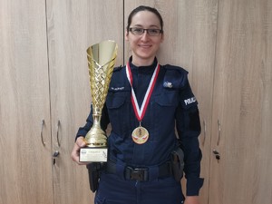 Zdjęcie przedstawia policjantkę z medalem i pucharem