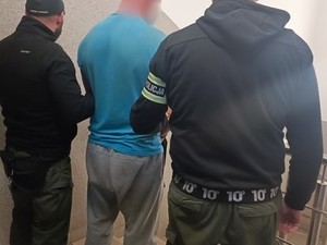 Na zdjęciu dwaj policjanci obróceni tyłem z zatrzymanym pośrodku