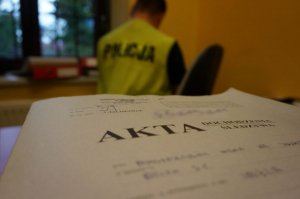 Akta śledztwa, a w tle siedzi policjant w kamizelce odblaskowej