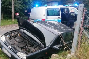 grafika-dzień, policyjny radiowóz z włączonymi sygnałami uprzywilejowania, uszkodzony skradziony VW Golf w rowie, pomiędzy pojazdami policjanci