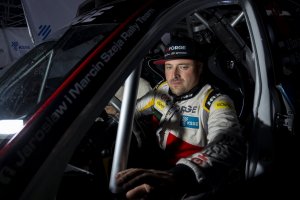 zdjęcie-kierowca Jarosław Szeja w stroju kierowcy wyścigowego, noc, siedzi za kierownicą samochodu wyścigowego