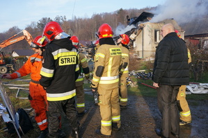 zdjęcie-dzień, funkcjonariusze straży pożarnej, w tle uszkodzony dom