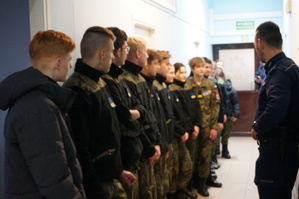 zdjęcie- młodzież z klasy mundurowej stoi na korytarzu i słucha policjanta
