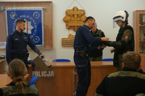 zdjęcie- policjant prezentuje umundurowanie ochronne, młodzież przymierza