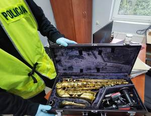 zdjęcie-policjant, pomieszczenie, sztuczne światło,otwarta walizka, odzyskany sprzęt muzyczny w walizce