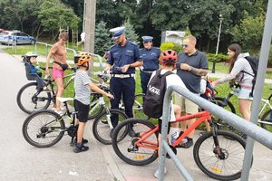 policjanci, dzień, osoby na rowerach, policjanci wręczają im lampki rowerowe