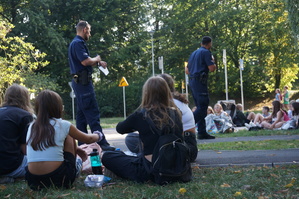 zdjęcie- dzień, słonecznie, dzieci siedzą na trawie i słuchają przemawiających policjantów