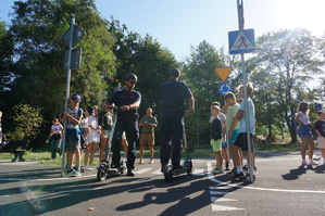 zdjęcie- dzień, słonecznie, dzieci i policjanci ćwiczą wspólnie jazdę na hulajnodze w miasteczku ruchu