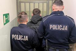 zatrzymany stoi przed celą z kratami, obok policjanci