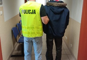 policjant trzyma za rękę osobę zatrzymaną, korytarz