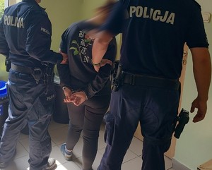 policjanci na korytarzu pilnują zatrzymanej kobiety, która ma kajdanki na rękach z tylu