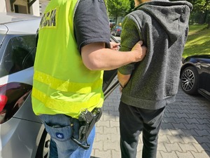 mężczyzna w kajdanach zespolonych na rękach i nogach w asyście policjantów