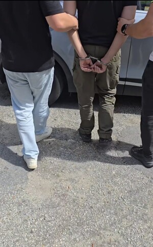 na zdjęciu podejrzany prowadzony do samochodu przez policjantów
