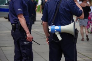 policjanci stoją tyłem  do fotografującego - jeden ma na ramieniu poasek z megafonem