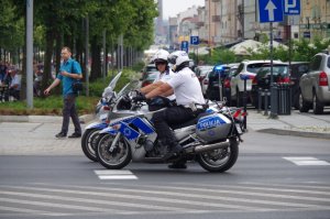 dwóch policyjnbych motocyklistów jedzie ulicą przed Placem Sienkiewicza