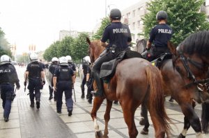tyłem policjanci z prwencji oraz dwóch jeźdźców policyjnych na koniach