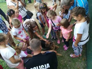Sara pies służbowy z wizytą u dzieci - dzieci wyciągają ręce by ją pogłaskać. Pies leży przy nogach swojego opiekuna