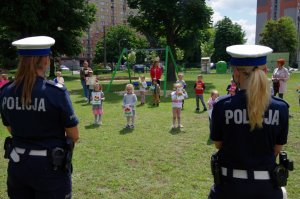 policjantki stoją na placu na zewnątrz przedszkola przed grupą dzieci, które recytują wiersz