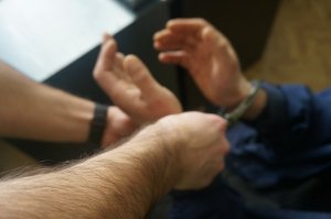 policjant zakłada zatrzymanemu kajdanki na ręce z przodu