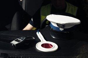 tarcza do zatrzymywania pojazdów, czapka policyjna i alkosensor leżące na podszybiu radiowozu