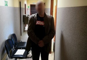 zatrzymany mężczyzna stoi na korytarzu w kurtce z kajdankami założonymi na ręce z przodu