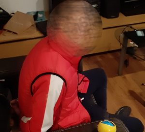 Zatrzymany mężczyzna w czerwonej kamizelce siedzi w fotelu z kajdankami na rękach
