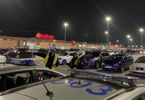policyjny radiowóz i policjanci na pierwszym planie, w tle samochody zaparkowane na parkingu pod centrum handlowym