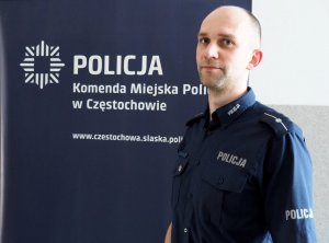 nominowany policjant pozuje do zdjęcia na tle napisu Komenda Miejska Policji w Częstochowie