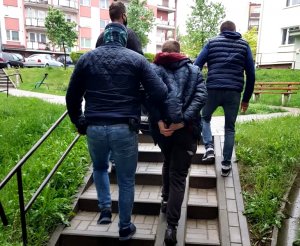 czterech nieumundurowanych policjantów prowadzi zatrzymanego mężczyznę po schodach na osiedlu mieszkaniowym