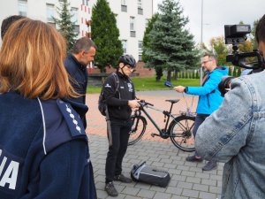 organizatorzy kampanii przed budynkiem Komendy Miejskiej Policji w  Częstochowie pokazują rodzaje zabezpieczeń do rowerów, przed nimi stoi kilku mężczyzn z lokalnych mediów