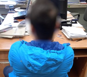 zatrzymany mężczyzna w niebieskiej kurtce siedzi na krzesełku tyłem do fotografującego