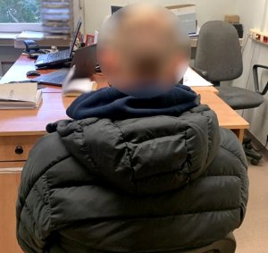 zatrzymany mężczyzna siedzi tyłem do fotografującego przodem do biurka