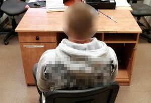 zatrzymany mężczyzna siedzi tyłem do fotografującego przodem do biurka