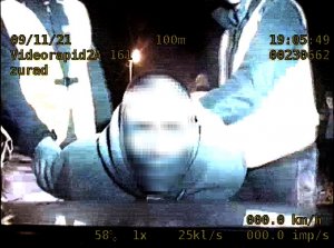 zatrzymany mężczyzna opiera się o maskę radiowozu, policjanci stoją za nim i zakładają mu kajdanki na ręce trzymane z tyłu