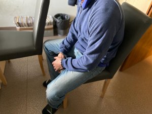 zatrzymany z kajdankami na rękach trzymanych z przodu siedzi na krześle podczas przesłuchania