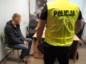 zatrzymany mężczyzna siedzi na krześle, obok stoi policjant w kamizelce odblaskowej