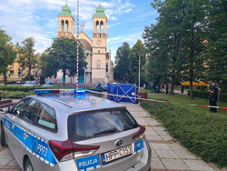 zdjęcie na pierwszym planie przedstawia radiowóz stojący w miejscu zabójstwa w Częstochowie na placu Orląt Lwowskich, na drugim planie rozwinięty parawan oraz grupa policjantów na miejscy zdarzenia