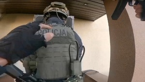 zdjęcie przedstawia rękę policjanta, który dotyka idącego przed nim policjanta oddziału kontrterrorystycznego trzymającego tarczę