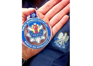 pamiątkowy medal trzymany na dłoni policjantki, w tle policyjna czapka