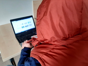 mężczyzna w czerwonej kamizelce z kapturem na głowie siedzi przed komputerem