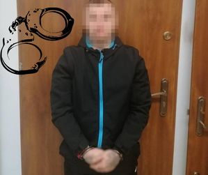na zdjęciu zatrzymany mężczyzna stoi przy drzwiach z kajdankami założonymi na ręce