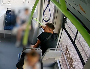 młody mężczyzna ubrany w czarna koszulkę z krótkim rękawem siedzi tyłem do kierunku jazdy w tramwaju